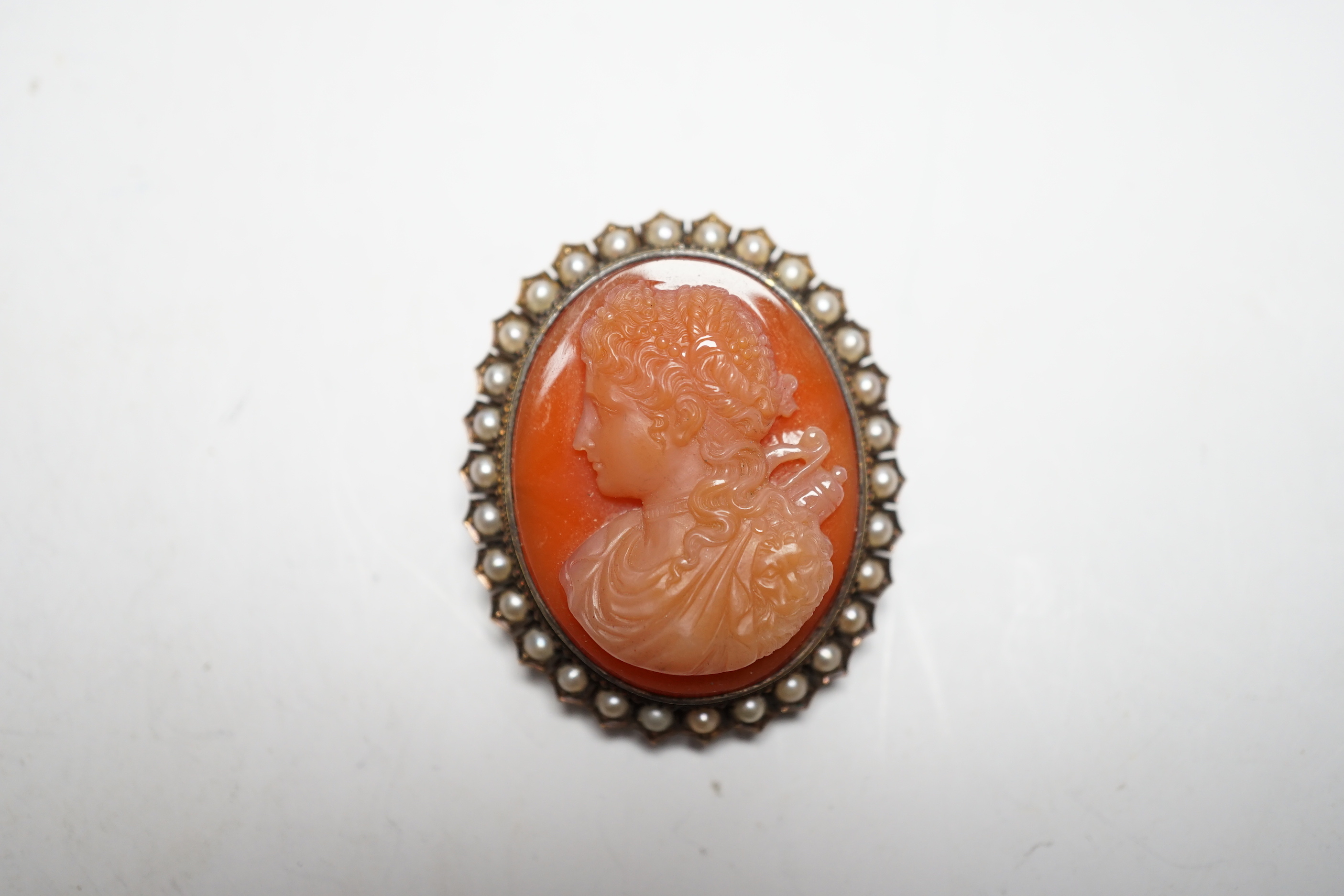 A Victorian yellow metal, and seed pearl mounted oval hardstone cameo pendant brooch, carved with the bust of a lady to dexter, 39mm.